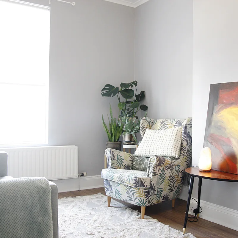 A quiet consulting room: an armchair by a bright window, plants and a painting