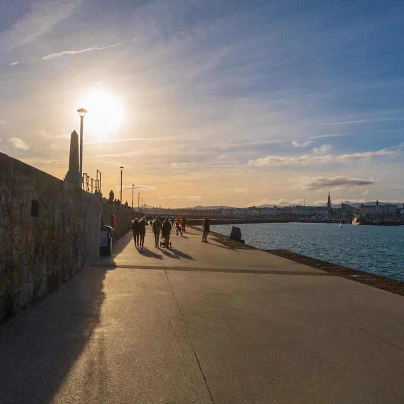Dún Laoghaire’s East Pier at sunset, people strolling towards the town